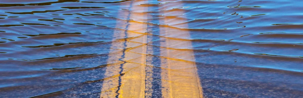 Photograph of a highway that is zoomed in on the double yellow lines. The highway is flooded with water.